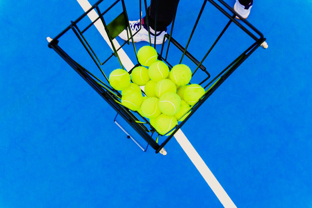 Кошик, повний жовтих тенісних м'ячів для тренувань тенісистів на синьому дворі
. - Фото, зображення
