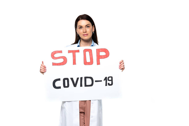 Brunette doctor in white coat holding placard with stop covid-2019 lettering isolated on white  - Fotografie, Obrázek