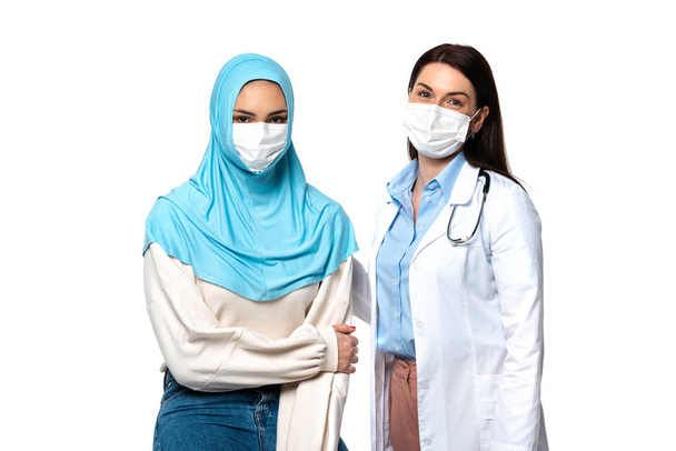 Muzułmański pacjent i lekarz w maskach medycznych patrząc na aparat odizolowany na białym  - Zdjęcie, obraz