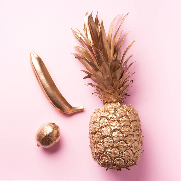 Creative layout. Gold pineapple, banana, lemon on pink background with copy space. Top view. Tropical flat lay. Exotic food concept, crazy trend. - Photo, image