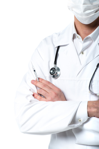 Widok lekarza w masce medycznej trzymającego strzykawkę, stojącego ze skrzyżowanymi ramionami odizolowanymi na biało  - Zdjęcie, obraz