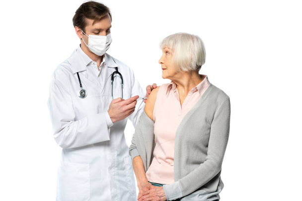 Senior Patient sieht Arzt in medizinischer Maske während Impfung isoliert auf weiß  - Foto, Bild