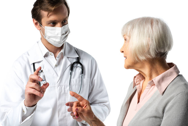 Doctor in medical mask holding vaccine near smiling patient pointing with finger isolated on white  - Photo, Image