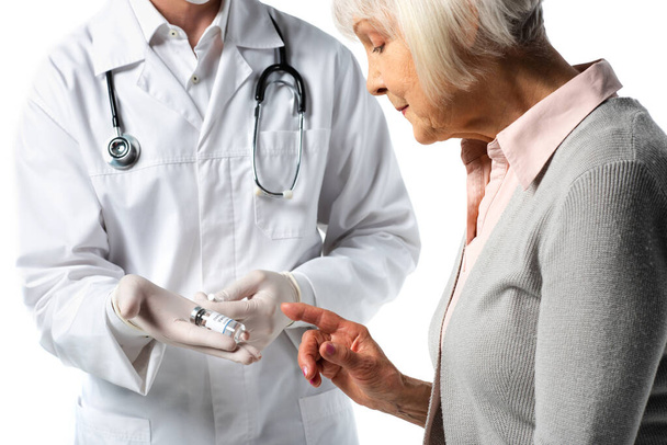 Starší pacient ukazující prstem na lékaře v latexových rukavicích s vakcínou a injekční stříkačkou izolovanou na bílém  - Fotografie, Obrázek