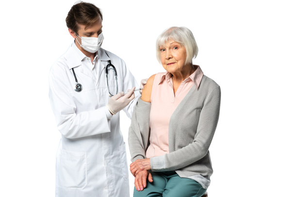 Idős beteg a kamerába néz, miközben az orvos a vakcina injekciót fehér alapon izolálja.  - Fotó, kép