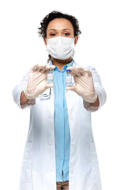 Koronavirüs aşısı olan kavanozlar, beyaz arka planı bulanık olan, tıbbi maskeli Afrikalı Amerikalı bir doktorun ellerinde.  - Fotoğraf, Görsel