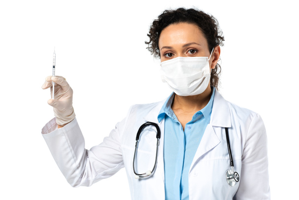 Médico afroamericano con máscara médica que sostiene jeringa con vacuna aislada en blanco  - Foto, Imagen