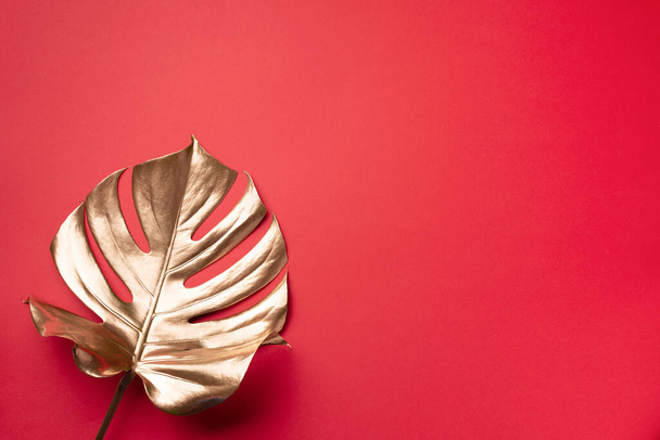 Floral minimal style concept. Exotic summer trend. Golden tropical palm monstera leaf on red color background. Shiny and sparkle design, fashion concept. - Fotó, kép