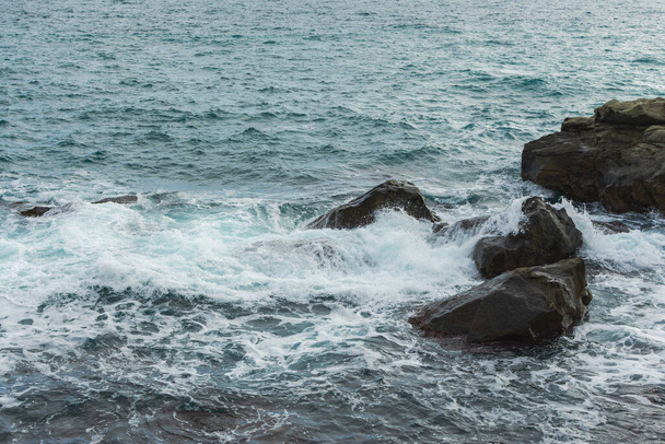 Turquoise sea stone beach, breaking waves on a cloudy spring day. Beautiful sea background. The concept of summer, vacation, travel. The purest clear sea water, large stones on the beach close-up - Photo, Image