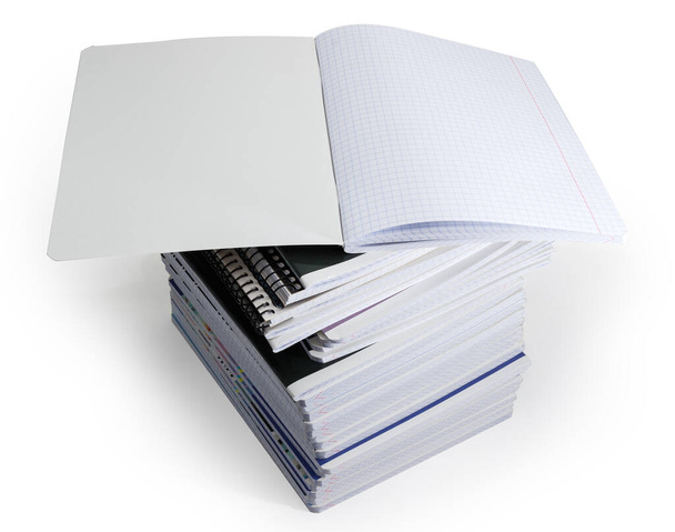 Открытая школьная тетрадь с листами квадратной бумаги лежит на большой стопке других различных толстых тетрадей упражнений на белом фоне - Фото, изображение