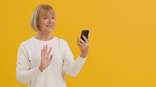 Beszéljen a távoli családdal. Boldog idős nő videó hívás rokonok, integetett kezét okostelefon és mosolygós - Felvétel, videó