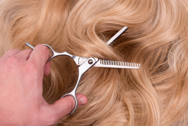 Friseur schneidet lange blonde Haare mit einer dünnen professionellen Schere. Trimmen gefärbter blonder Locken in Salons, Friseursalons, Haarpflege- und Schönheitsprodukten - Foto, Bild