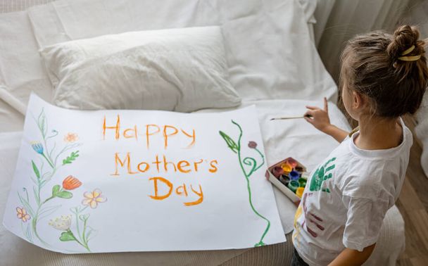 Menina pinta cartão de saudação para a mãe no Dia das Mães com a inscrição Dia da mãe feliz e flores. - Foto, Imagem