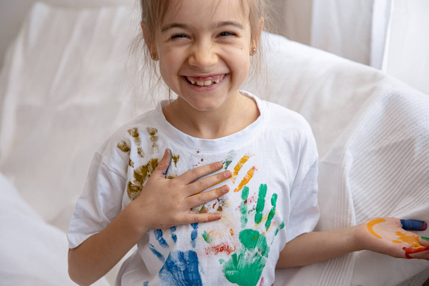 小さな女の子がTシャツの上に描かれたヤシの木の痕跡を残します。子供の創造性と芸術. - 写真・画像