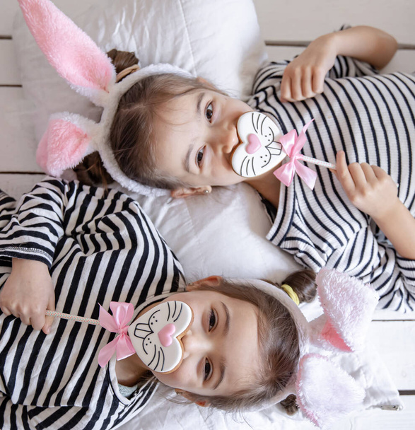 Веселі маленькі сестри з пасхальними пряниками у вигляді облич кролика і з вухами кролика
. - Фото, зображення