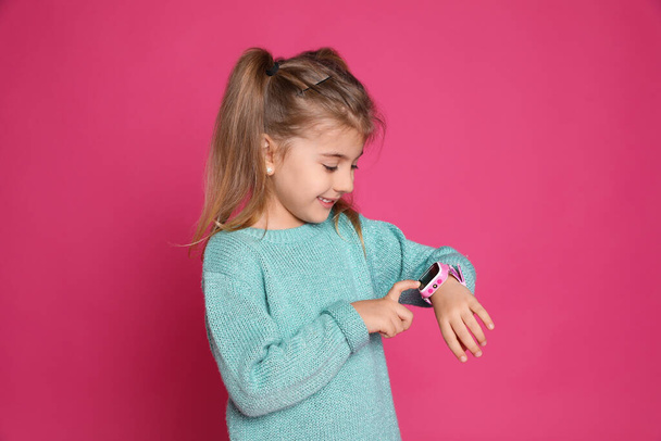 Little girl with smart watch on pink background - 写真・画像