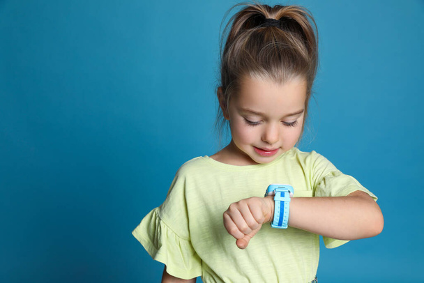 Little girl with smart watch on light blue background, space for text - Fotoğraf, Görsel