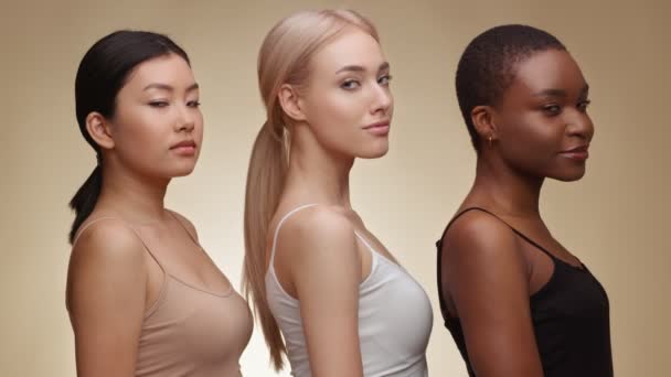 Beauté interraciale. Portrait de profil de femmes mixtes tournant les visages vers la caméra et souriant, posant sur fond beige - Séquence, vidéo