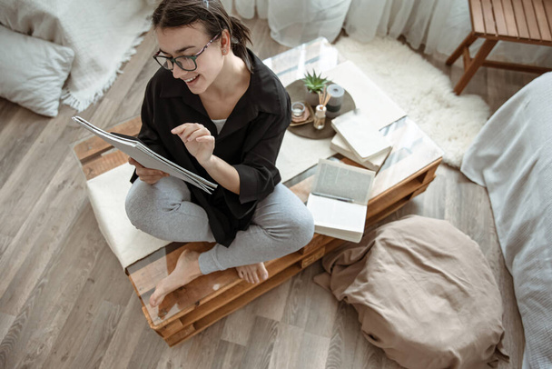 Attraente ragazza felice a casa seduta con un notebook e penna tra i libri - Foto, immagini