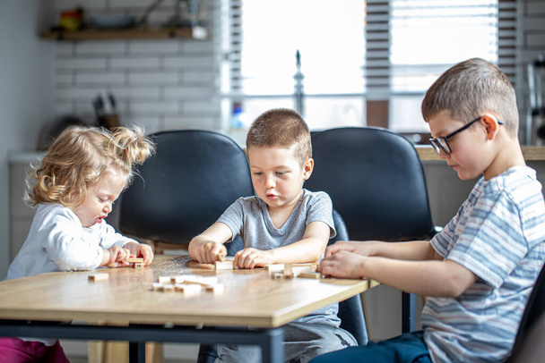 Small children play a board game with wooden cubes at home in the kitchen. - Photo, Image