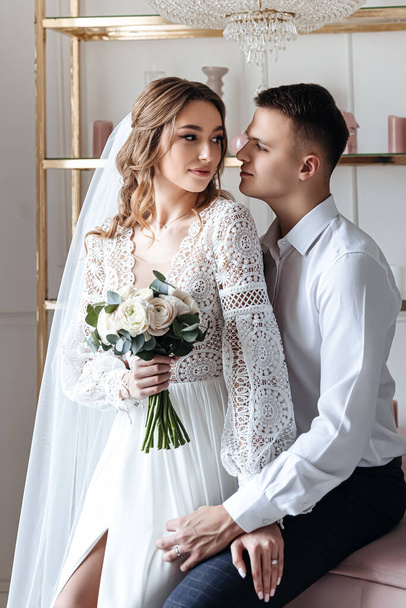 The groom gently hugs the bride in a beautiful lace dress with a bouquet of fresh flowers. Wedding photo session in the studio. - Photo, image