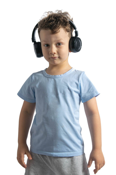Ένα όμορφο ευρωπαϊκό αγόρι ακούει μουσική με ακουστικά. Μουσικός εραστής από παιδί. Ντι Τζέι. Απομονωμένα σε λευκό φόντο. - Φωτογραφία, εικόνα