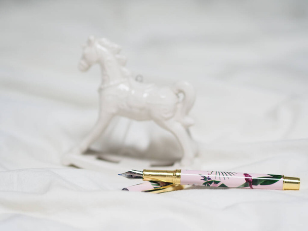 A beautiful ornamented ink pen by the white small horse statue on white background - Fotó, kép
