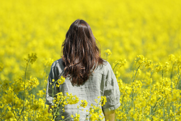 Back view of a woman walking in a yellow flowered field in spring season - Fotoğraf, Görsel