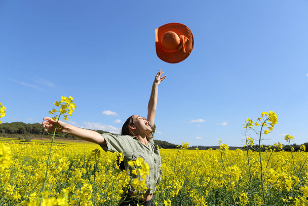 Happy woman throwing pamela celebrating vacation in a yellow flowered field in spring - Photo, image