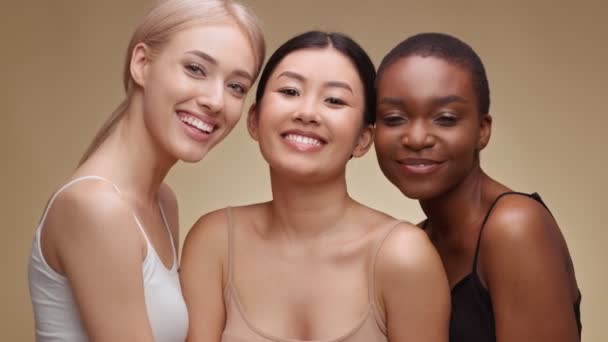 Üç mutlu çoklu etnik bayanın stüdyo portresi kameraya gülüyor, arkadaşlığın tadını çıkarıyor, bej arka planda sarılıyorlar. - Video, Çekim