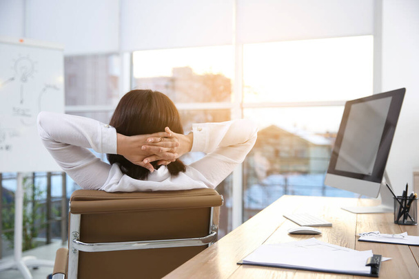 Женщина расслабляется в офисном кресле на рабочем месте, вид сзади - Фото, изображение