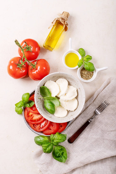 Home made healthy meal concept: cherry tomatoes, mozzarella balls, spices, olive oil and fresh basil. Mozzarella salad over white texture background. Copy space. Top view, flat lay - Valokuva, kuva