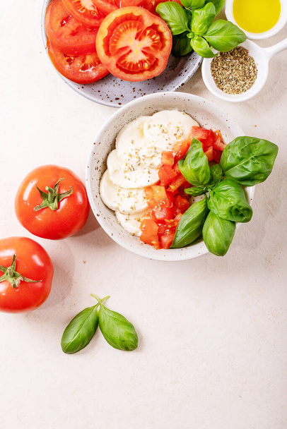 Home made healthy meal concept: cherry tomatoes, mozzarella balls, spices, olive oil and fresh basil. Mozzarella salad over white texture background. Copy space. Top view, flat lay - Foto, afbeelding