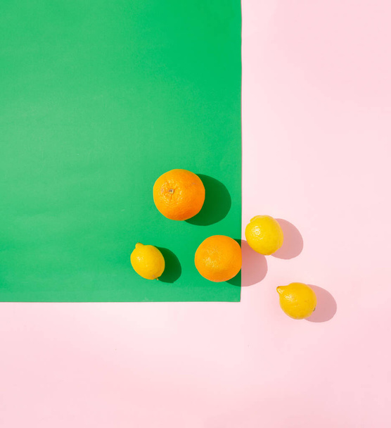 Творчий макет з оранжевими шматочками та лимонами на пастельному зеленому та рожевому тлі. Концепція мінімальних сонячних денних тіней
. - Фото, зображення