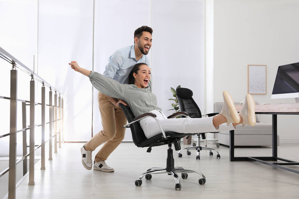 Office employee giving his colleague ride in chair at workplace - Valokuva, kuva