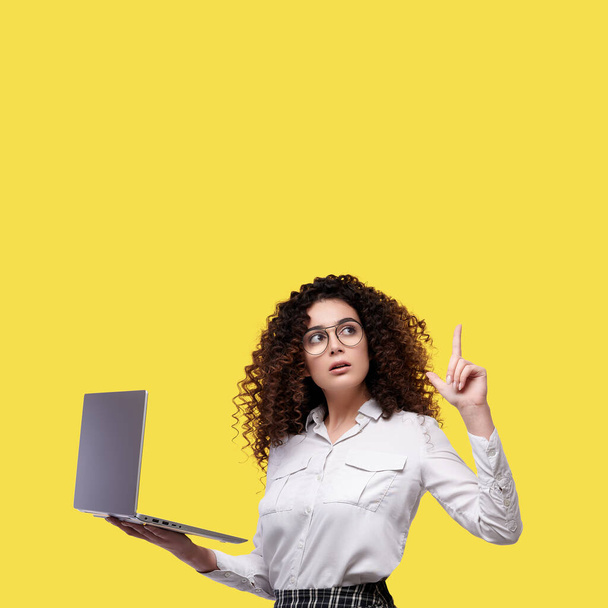 Zaskoczony biały bizneswoman w białej koszuli i okularach z laptopem i wskazując palcem na żółtym odizolowanym tle. - Zdjęcie, obraz