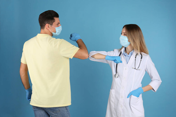Doctor and patient doing elbow bump instead of handshake on light blue background. New greeting during COVID-19 pandemic - Photo, Image