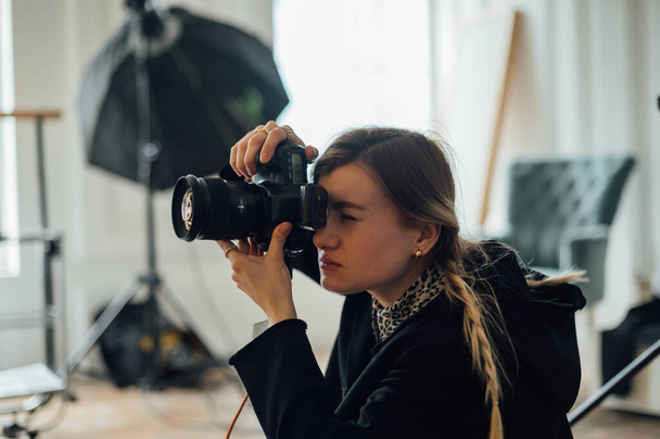 Retrato de cerca de una fotógrafa haciendo una sesión de fotos en un estudio fotográfico, mirando al visor de la cámara y presionando el botón del obturador. - Foto, imagen