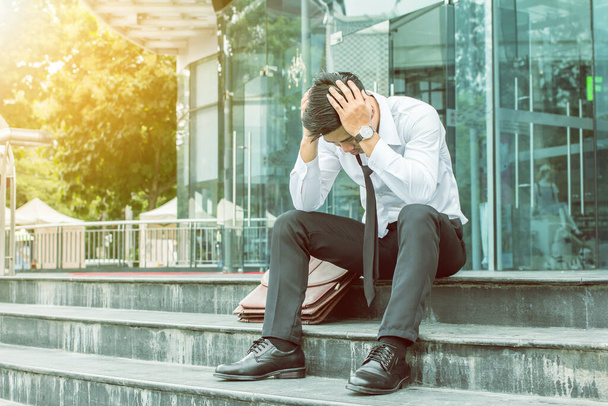 Asiático joven de negocios sentado en las escaleras en la oficina, estresado, obligado a salir de la oficina en cualquier lugar soleado. - Foto, Imagen