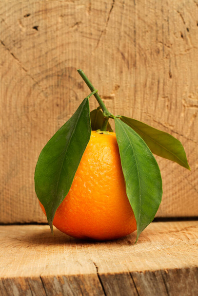 Une orange avec des feuilles vertes sur une tranche de tronc d'arbre - Photo, image