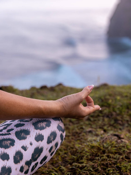 Close up gyan mudra. Die Hälfte der Lotus Pose, Padmasana. Konzentrieren Sie sich auf Finger. Yoga-Retreat. Frau sitzt auf Gras und praktiziert Yoga mit Gyan Mudra. Selbstversorgungskonzept. Klippe von Uluwatu, Bali, Indonesien - Foto, Bild