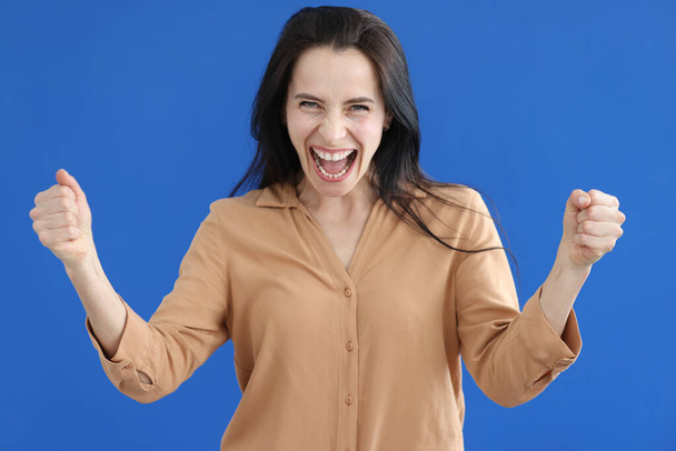 Zufriedene Frau mit gefalteten Fäusten schreit auf blauem Hintergrund - Foto, Bild