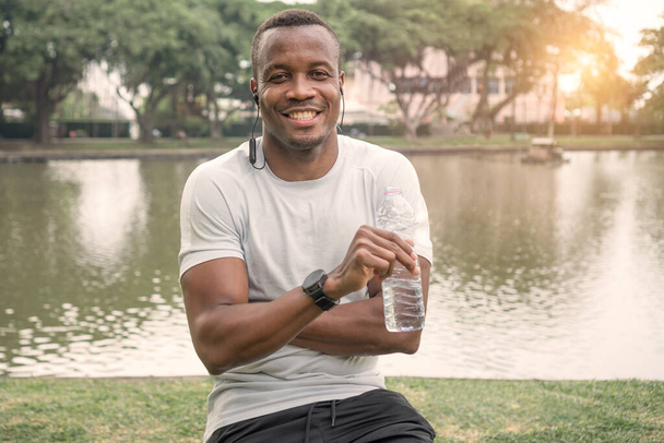 portré afro-amerikai férfi sportoló mosolyogva boldog. Sportember inni vizet pihenni a folyón edzés után. izmos fiatalember sportruházatban, magabiztosan nevet. koncepció Egészségügy, szabadtéri testmozgás - Fotó, kép