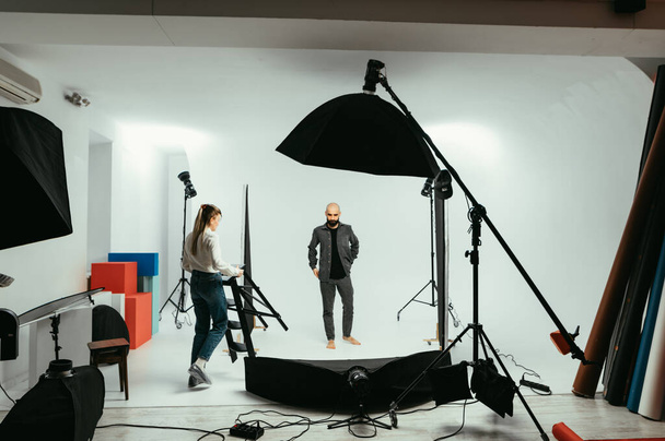 Foto de bastidores, fotógrafa e modelo masculina trabalhando em estúdio de fotografia em um fundo branco - Foto, Imagem