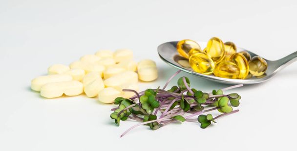 Természetes vitamin kontra mesterséges farmakológiai vitamin koncepció. Mikrozöld, tabletták és kanál kapszulával fehér alapon - Fotó, kép