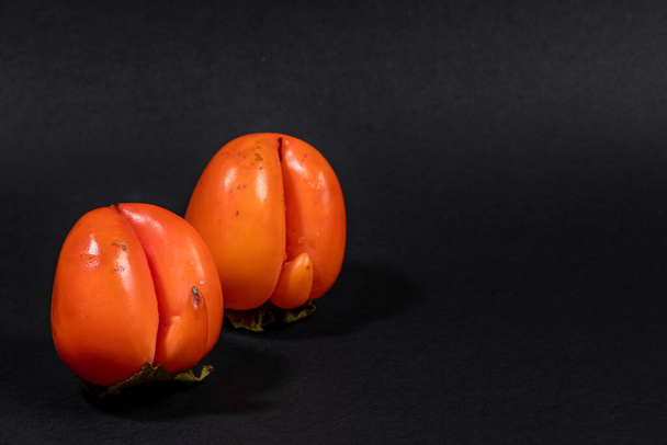 Two non-standard ugly ripe orange persimmons on black background. Fresh natural healthy organic fruits. Zero waste food, reasonable and sustainable consumption concepts. Copy space for text. - Φωτογραφία, εικόνα
