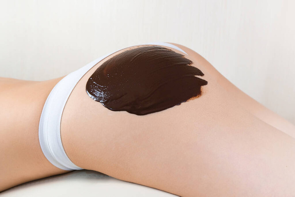 Skin rejuvenation, chocolate wrap, body mask. Applying chocolate to the young women buttocks - Fotografie, Obrázek