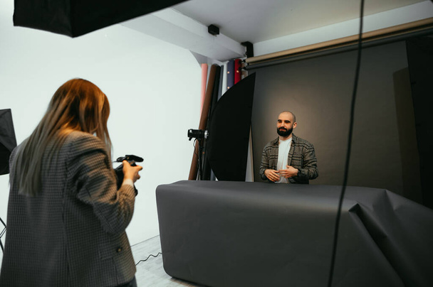 Fotografo donna fa ritratti per l'uomo barbuto su sfondo grigio. Foto dietro le quinte - Foto, immagini