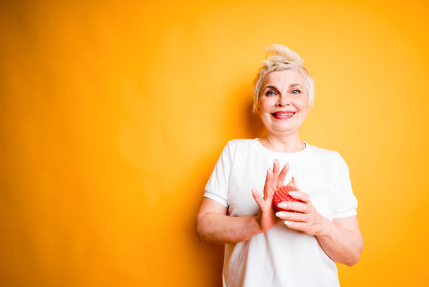 Happy elderly woman in a white t-shirt holds a massage ball to relax the muscles and runs it on her palms - Photo, Image