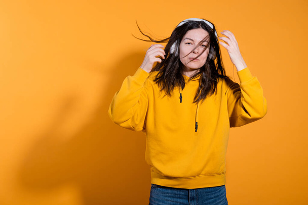Happy dancing music lover. A young woman in a yellow hoodie with white wireless headphones, - Fotografie, Obrázek
